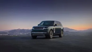 Dark green Range Rover Electric parked against a scenic mountain backdrop at sunset.