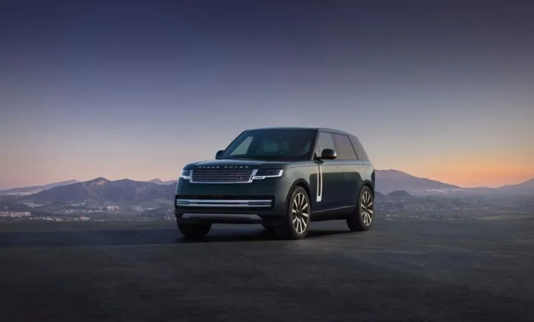 Dark green Range Rover Electric parked against a scenic mountain backdrop at sunset.