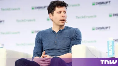 Sam Altman speaks on stage at a TechCrunch event wearing a blue shirt.