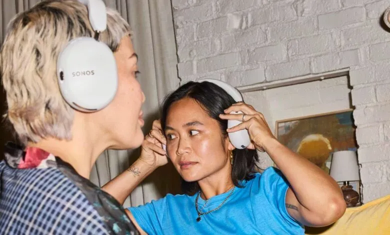 Two women wearing white Sonos Ace over-ear headphones indoors.