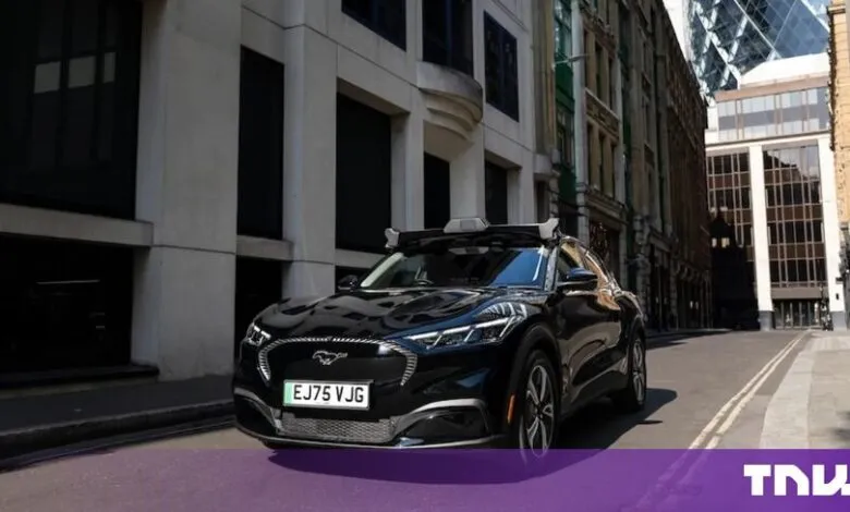 Black autonomous Wayve robotaxi parked on a narrow London street lined with historic and modern buildings.