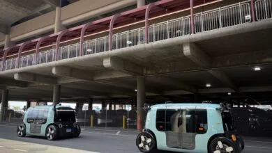Two autonomous Zoox robotaxis parked under a concrete parking structure.