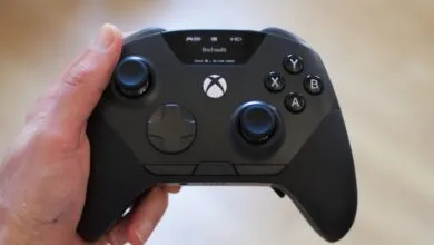 A person holding a modern black Xbox controller with an integrated display screen.