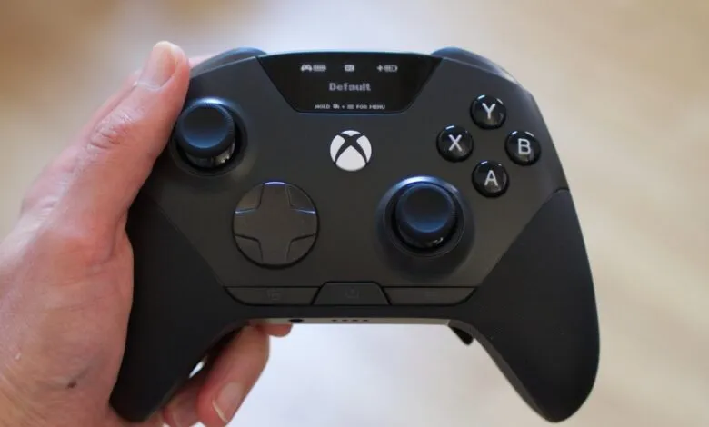 A person holding a modern black Xbox controller with an integrated display screen.