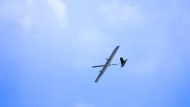 A sleek model airplane soaring gracefully through a bright blue sky with soft white clouds.