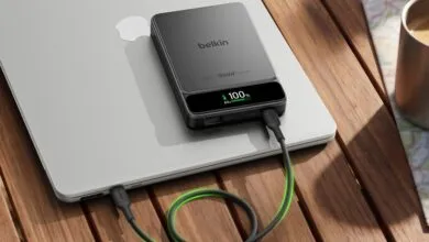 Belkin portable power bank resting on a silver laptop on a wooden outdoor table.