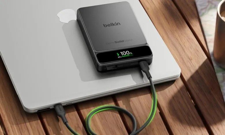 Belkin portable power bank resting on a silver laptop on a wooden outdoor table.