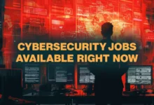 Silhouette of a professional overlooking multiple computer screens glowing with red cybersecurity data.
