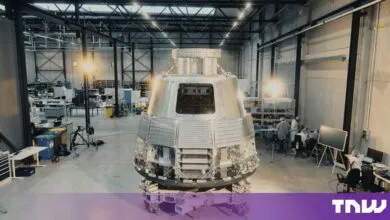 Large metallic space capsule undergoing assembly inside a modern manufacturing warehouse.