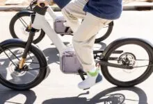 A person riding a modern white electric bicycle on a paved path outdoors.