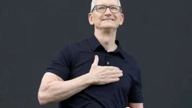 Apple CEO Tim Cook smiling warmly with his hand placed on his chest against a dark backdrop