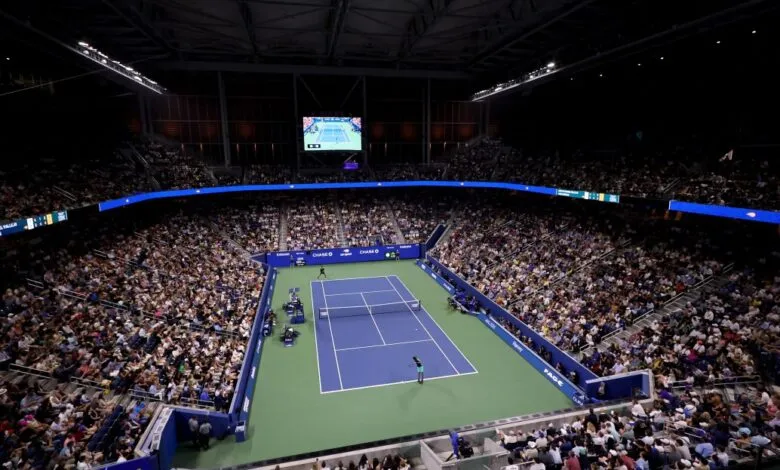 High-angle view of a tennis match inside a large, crowded indoor stadium under bright lights.