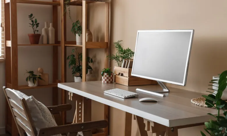 Minimalist wooden home office desk with computer, keyboard, and surrounding houseplants.