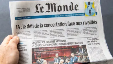 A hand holds the French newspaper Le Monde featuring headlines about AI and politics.