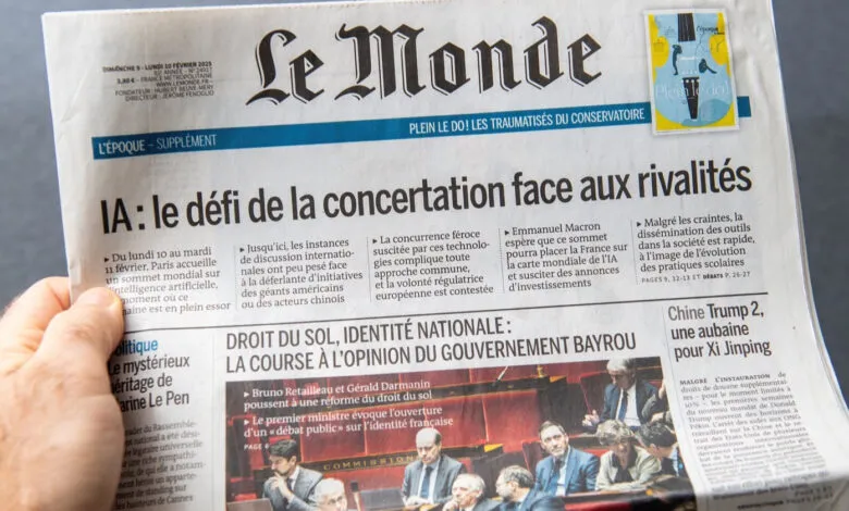A hand holds the French newspaper Le Monde featuring headlines about AI and politics.