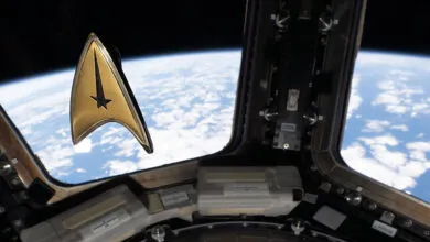 A gold Star Trek command insignia pin floats inside a spacecraft window overlooking Earth's horizon.