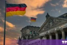 German flags wave proudly atop the historic Reichstag building in Berlin during a dramatic sunset.