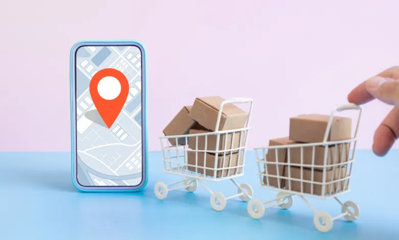 Smartphone with map location pin next to mini shopping carts filled with cardboard boxes.