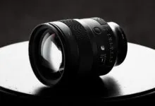 Close-up of a sleek black camera lens resting on a dark circular surface against a moody background.