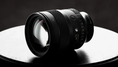 Close-up of a sleek black camera lens resting on a dark circular surface against a moody background.