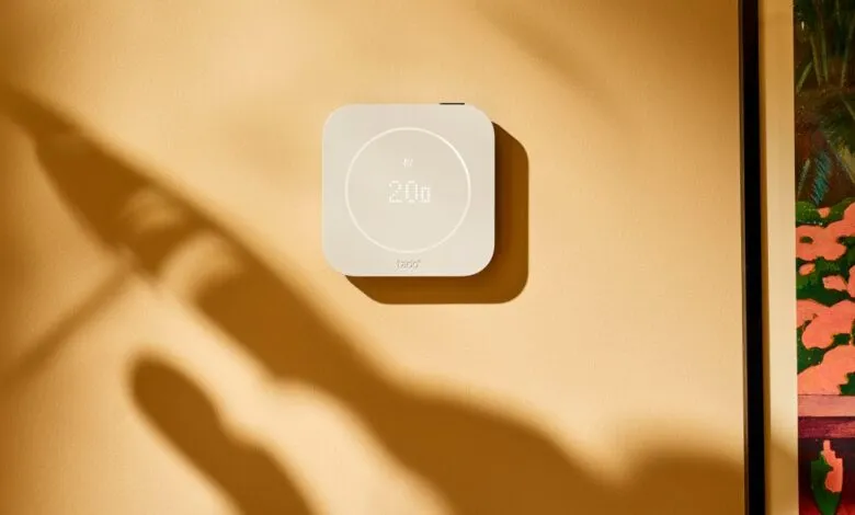 Modern white smart thermostat mounted on a warm beige wall with soft leaf shadows.