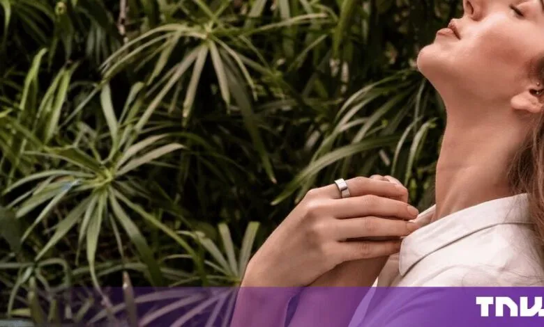 A woman wearing a sleek Ultrahuman smart ring while relaxing outdoors with lush green foliage