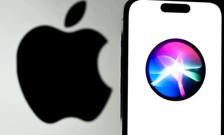 Close-up of an iPhone displaying the Siri app icon, with a blurred Apple logo in the background.