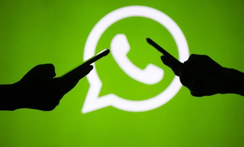Silhouetted hands hold phones in front of a large WhatsApp logo on a bright green background, symbolizing global communication.