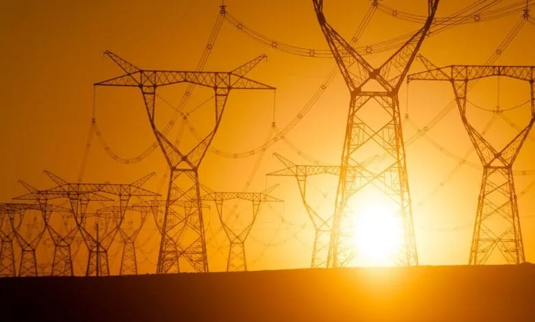 Silhouetted power lines at sunset; the sun glows brightly behind them.
