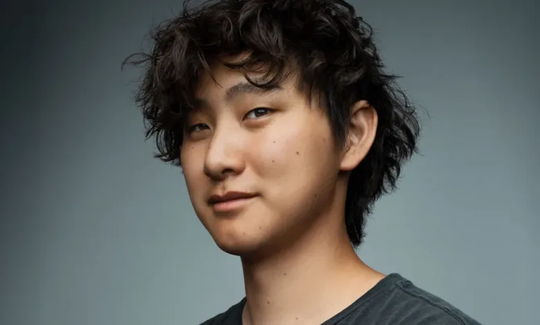 Close-up portrait of a young man with dark, curly hair, looking slightly off-camera with a subtle smile.