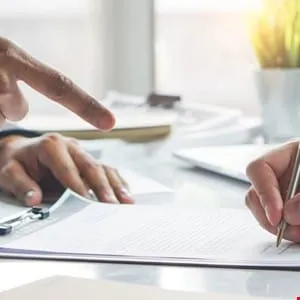 Close-up of hands signing a document, one hand pointing to the document.