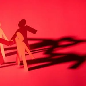 Paper chain figures holding hands cast dramatic shadows on a red background.