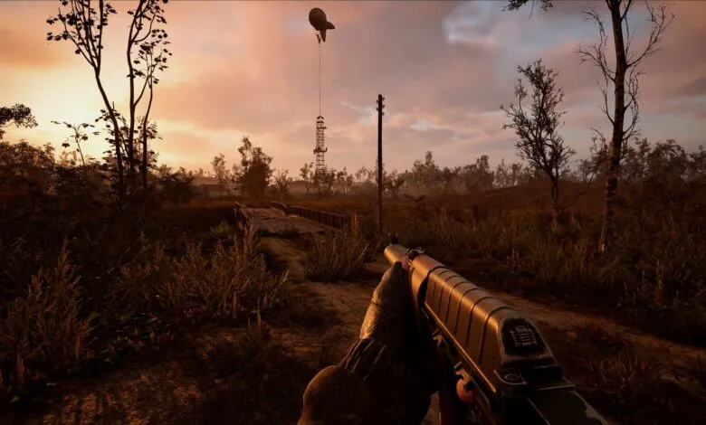 First-person view of a video game, player holding a rifle, aiming at a bridge and tower with a weather balloon at sunset.