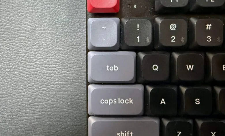 Close-up of a keyboard's top-left corner, showing keys like 'tab' and 'caps lock' in gray, contrasted against black keys and a gray leather surface.