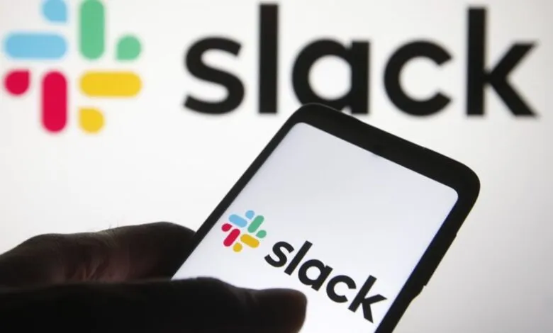 Close-up of a smartphone displaying the Slack logo and app, with the larger Slack logo blurred in the background.