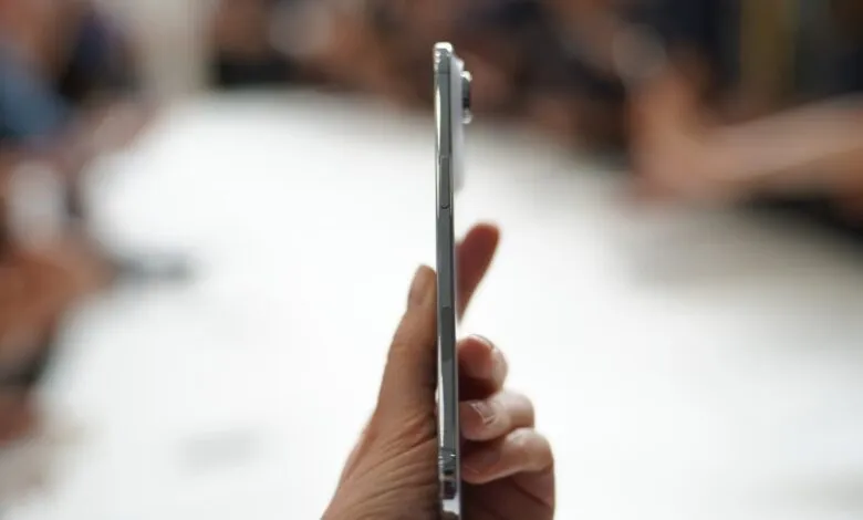 Close-up of a person's hand holding a silver smartphone, showcasing its side profile and buttons.