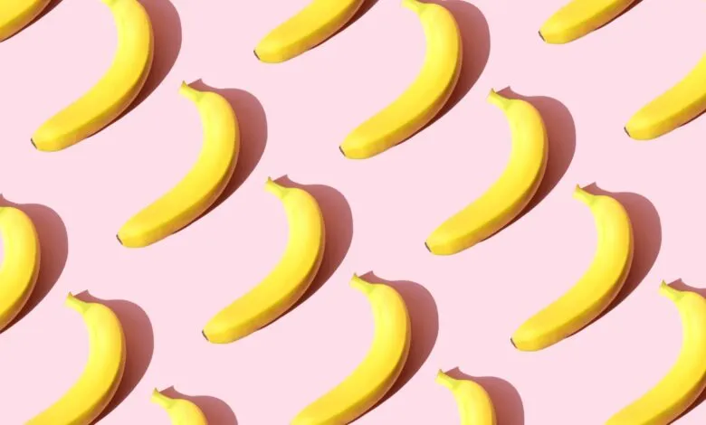 Repeating pattern of ripe yellow bananas arranged diagonally on a pink background.