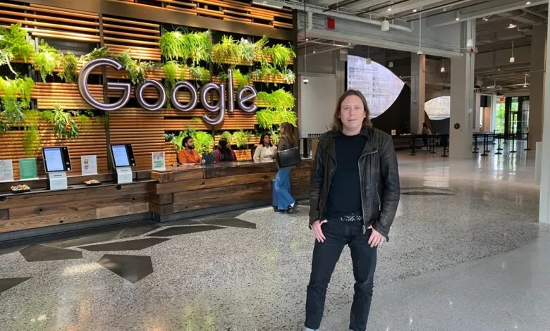 Person standing in Google's modern lobby, featuring a large illuminated Google logo and a living wall.