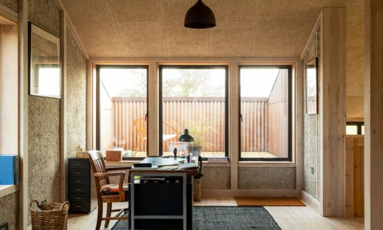 Home office with hempcrete walls, large windows overlooking a patio, and a simple desk.