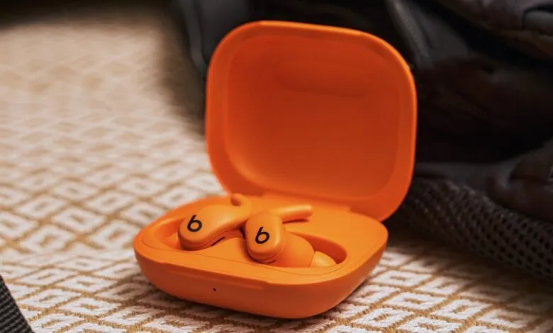 Bright orange Beats earbuds and charging case resting on a textured surface.