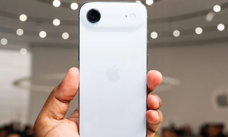 Close-up of a person holding a white iPhone with a prominent camera system on the back.