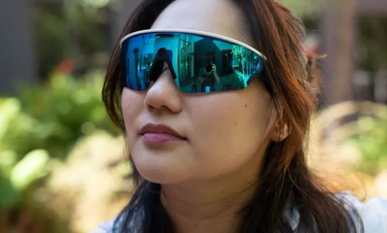 Woman wearing futuristic mirrored blue sunglasses reflecting a photographer and building.