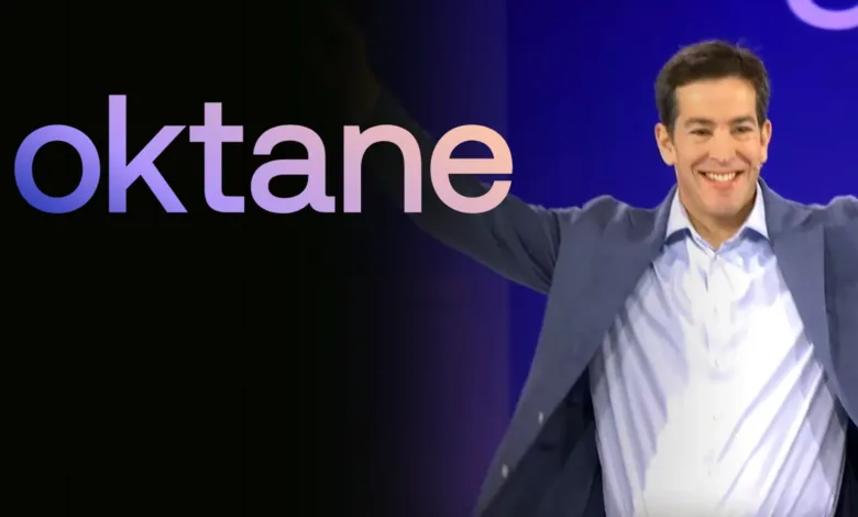 Todd McKinnon smiles broadly on stage with arms outstretched, with the Okta logo behind him.