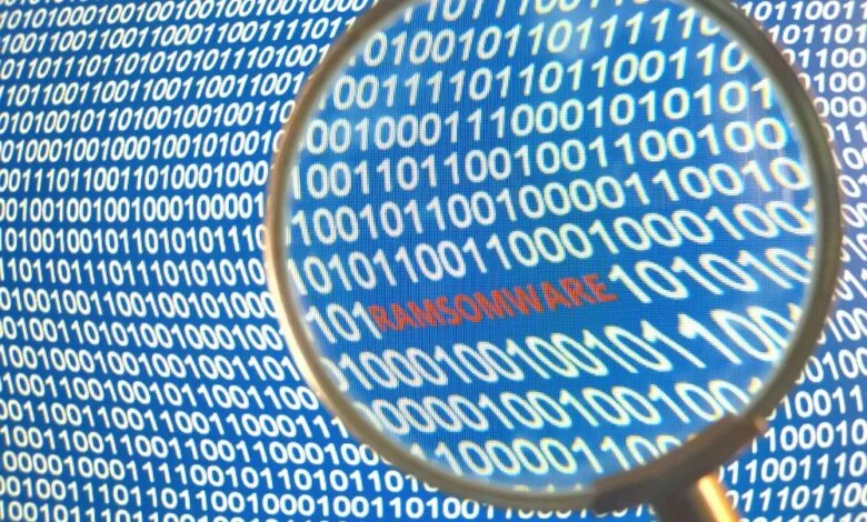 Close-up of a magnifying glass over binary code revealing the word 'Ransomware' in red.