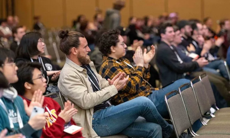 Audience members clapping at a conference or presentation, seated in rows.