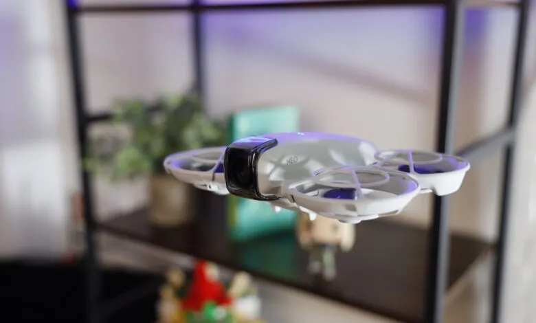 Close-up of a white drone with a camera and 'NEO' logo, hovering indoors.