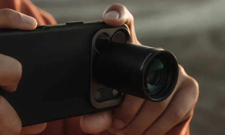 Close-up of hands holding an iPhone with a Sandmarc telephoto lens attached.