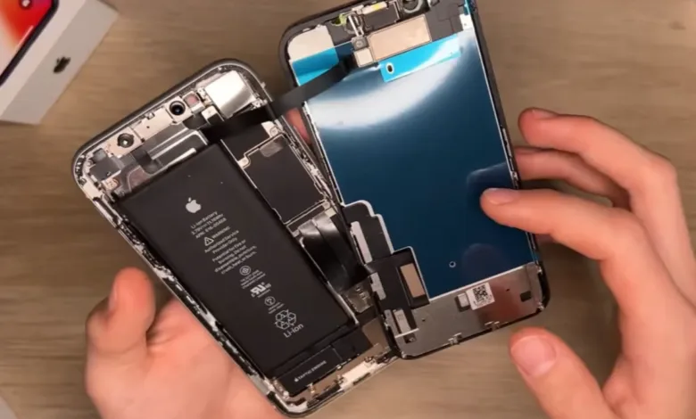 Hands holding a disassembled iPhone, showing the battery and internal components.