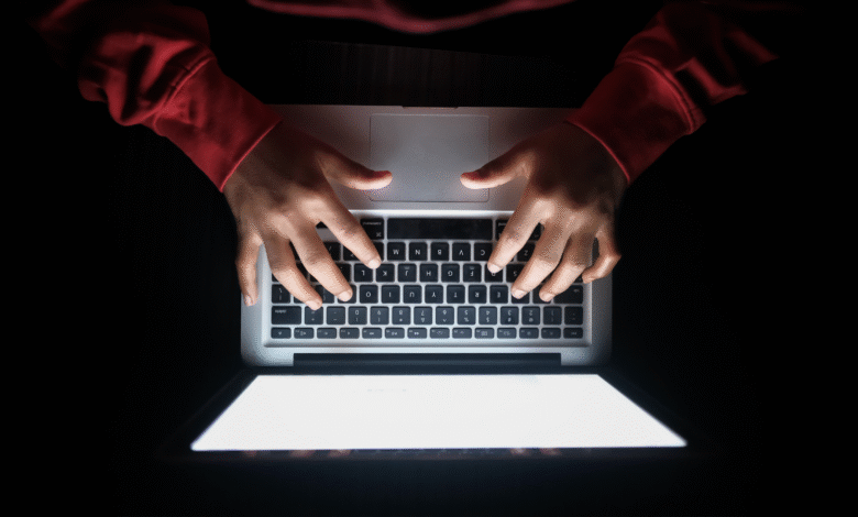 Overhead view of hands typing on a laptop keyboard in a dark room.