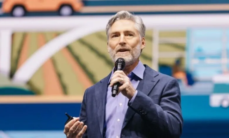 Man with gray hair and beard speaking into a microphone on stage.